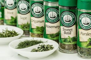 Assorted dried herbs in branded spice jars with bowls of loose herbs in the foreground.