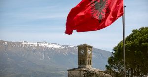 Iconic view of Gjirokaster Fortress featuring the Albanian flag and a clock tower under a blue sky.